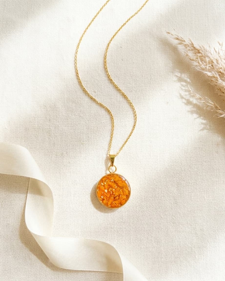 Pingente circular de resina com flocos dourados sobre superfície de pedra bege