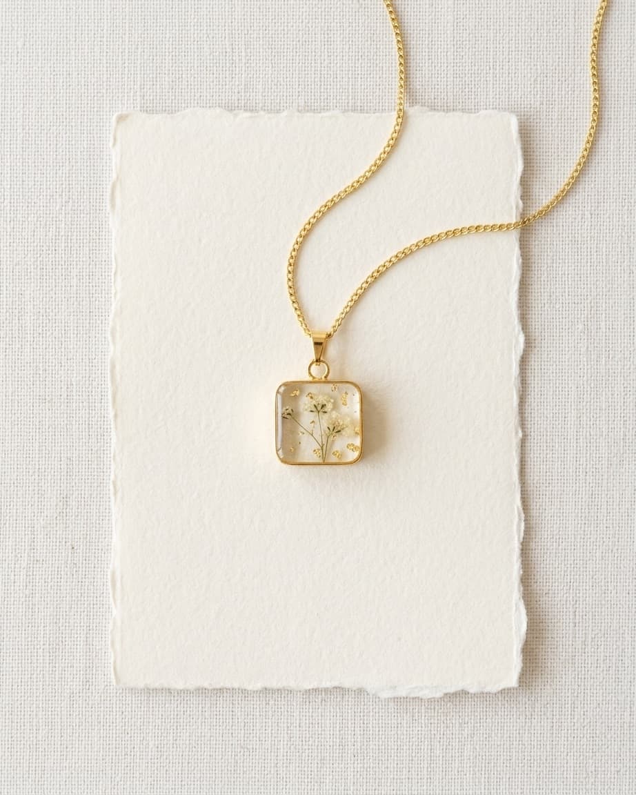 Pingente retangular de resina contendo flores brancas secas sobre tecido de seda branco